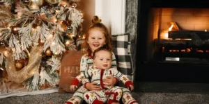 크리스마스 트리와 벽난로가 피워져 있으며 여자아이가 남자아이로 보이는 아기를 안고 있습니다.