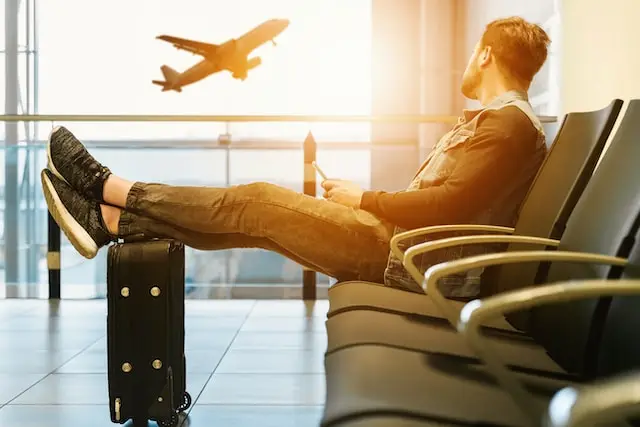 십이신살 역마살 - 공항 라운지에 한 남자가 다리를 쭉 뻗고 앉아서 이륙하는 비행기를 쳐다보고 있습니다.