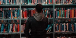 편인 2 책장 앞에 한 남자가 서서 책을 고르고 서 있습니다.