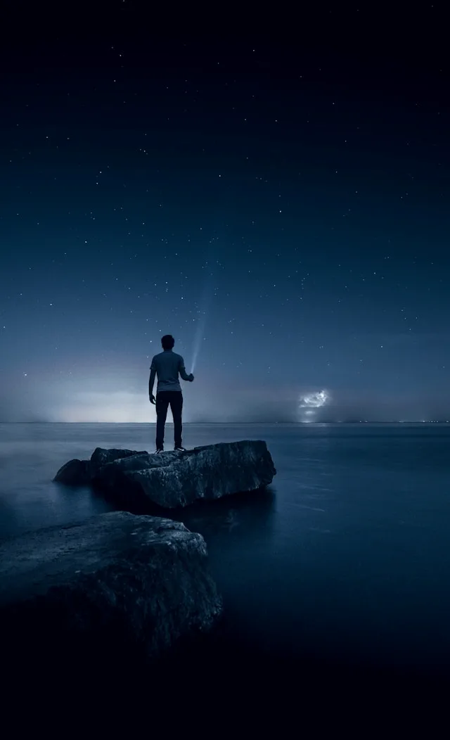 교신성 - 다른 사람과 어울리기 힘든 신살을 나타냅니다. 사진에 혼자 밤하늘을 보고 있는 남자가 바닷가의 돌위에 서 있습니다.